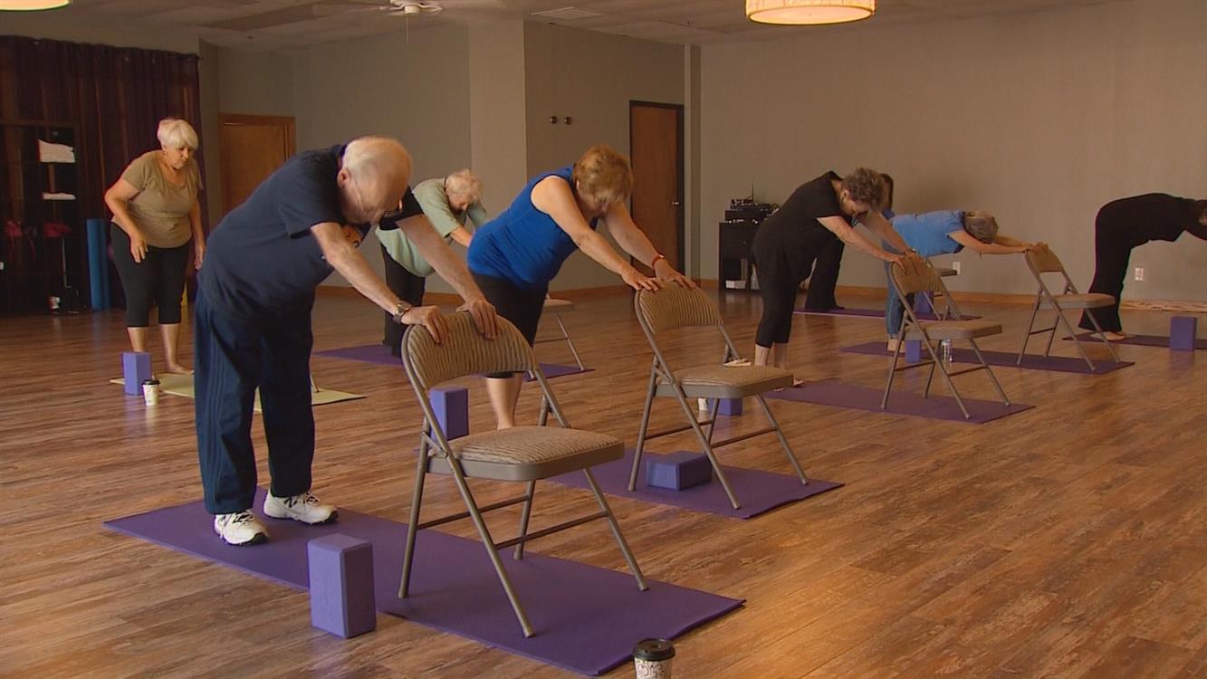 Mixed age people perform chair yoga